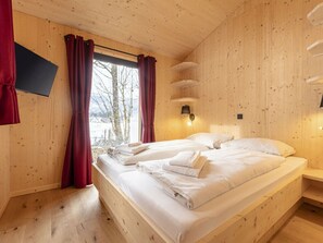 Un dormitori de cabana de fusta amb un llit, cortines, una làmpada penjada a la paret i una finestra amb vistes.