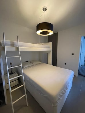 Een slaapkamer met een stapelbed, een bureau met lamp en een moderne hanglamp.