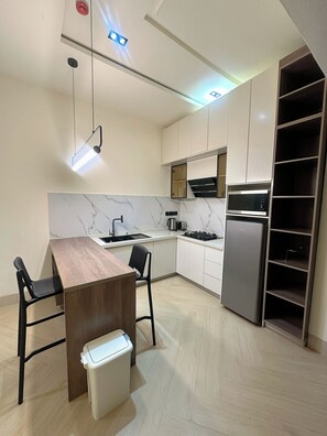 Une cuisine moderne avec une table à manger en bois, des chaises noires, une cuisinière encastrée et un réfrigérateur en acier inoxydable.
