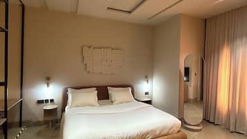 A modern hotel room with a large bed, a mirror, a wall-mounted light fixture, and a ceiling light.