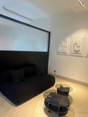Un salon moderne avec un canapé noir, une table basse en verre et des œuvres d’art accrochées au mur.