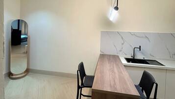 A modern kitchen with a marble countertop, a wooden dining table, two black chairs, and pendant lighting.