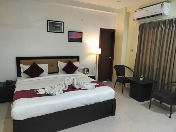 A hotel room with a bed, a desk, a chair, an air conditioning unit, and two framed pictures on the wall.
