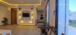 Um interior moderno com TV central, iluminação embutida e área de jantar com bancos.