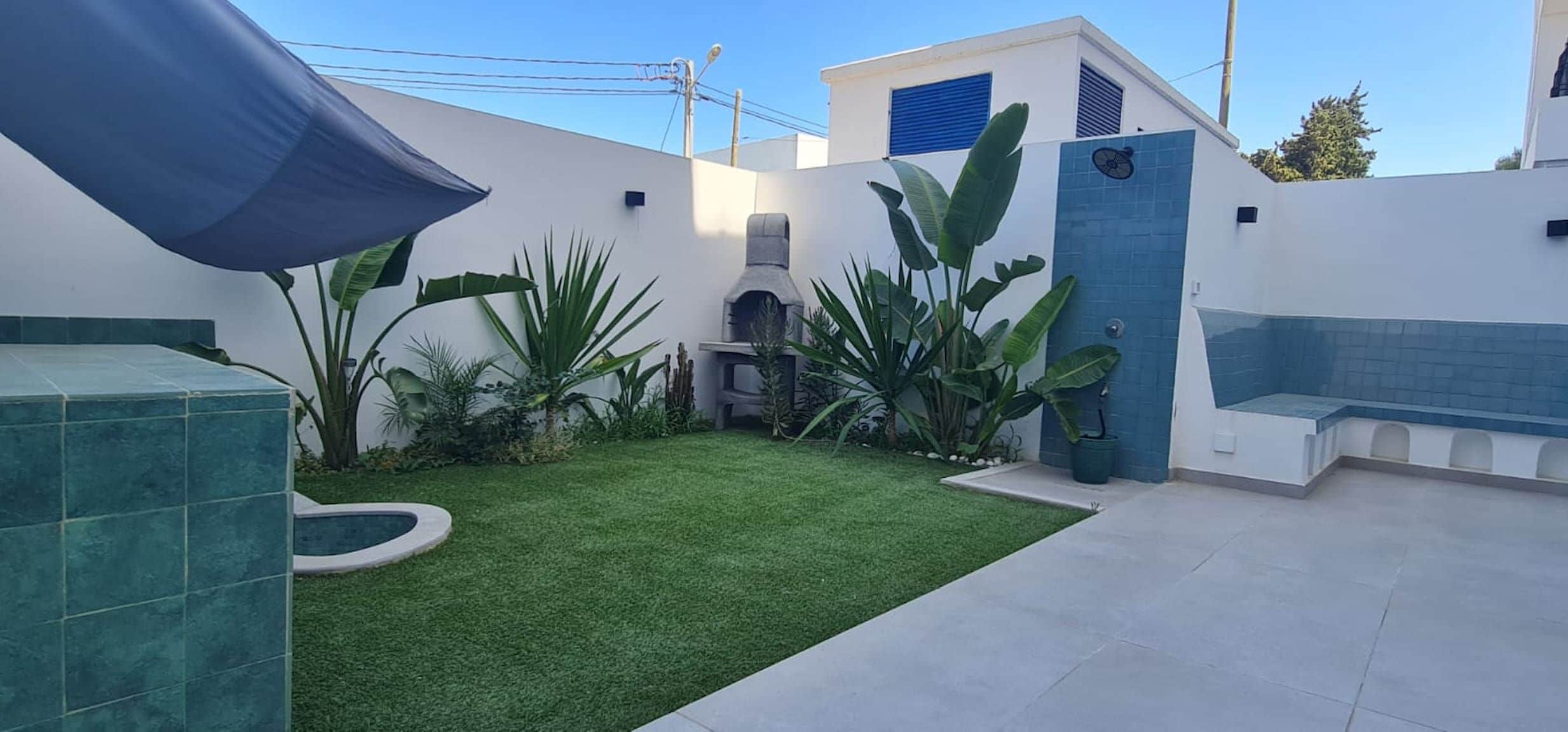 Un patio con césped artificial, una pequeña piscina y diversas plantas tropicales.