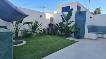 Un patio con césped artificial, una pequeña piscina y diversas plantas tropicales.
