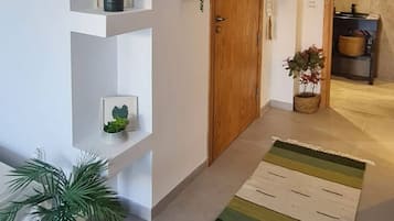 A hallway with a wooden door, a white wall with shelves, and a striped rug.