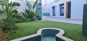Un espacio exterior moderno con césped artificial, una piscina pequeña y plantas en macetas.