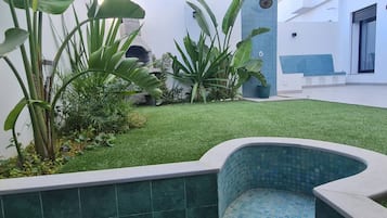 A courtyard with artificial grass, a tiled pool, and various plants.