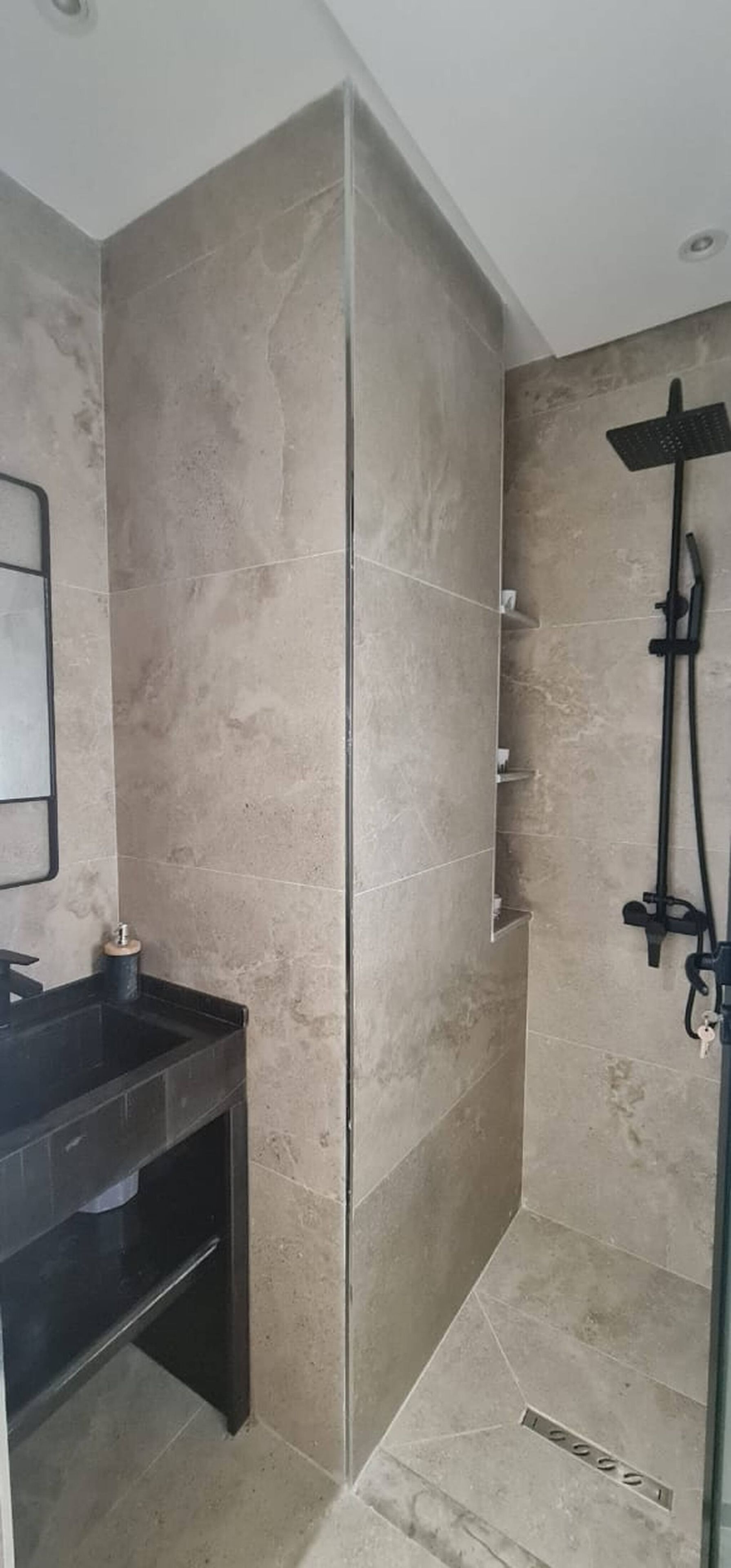 Une salle de bain avec une douche à parois de verre, un lavabo noir et un miroir.