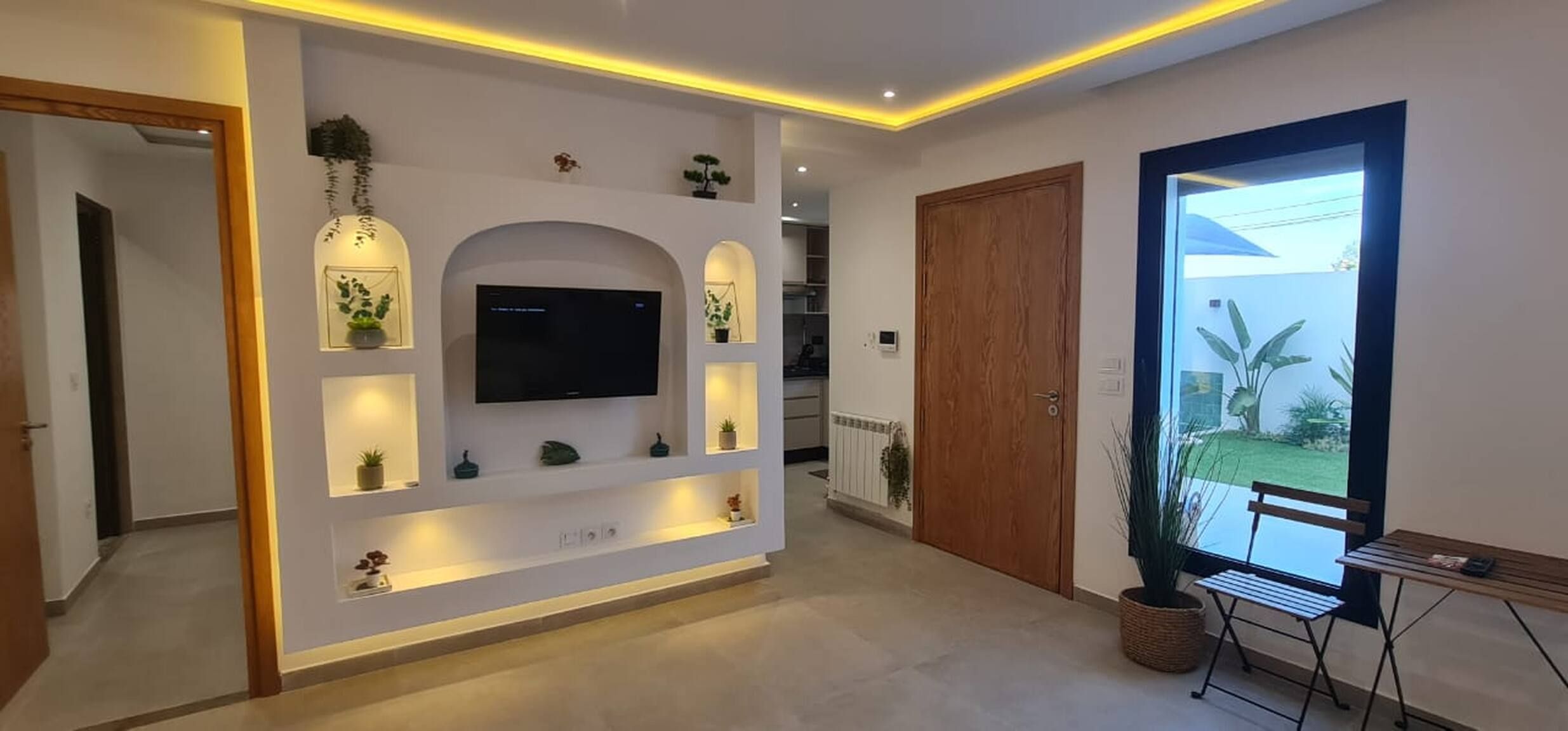 Ein modernes Wohnzimmer mit Flachbildfernseher, Einbauleuchten und Blick ins Freie.