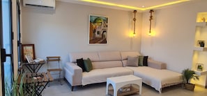 Una sala de estar con un sofá, una mesa de centro, una mesita con una silla y un cuadro en la pared.