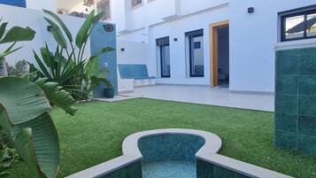 Un edificio moderno con piscina, césped artificial verde y plantas tropicales.