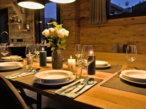 A wooden dining table set with plates, cutlery, glasses, and candles, with a vase of flowers in the center. - One-bedroom Cabin (Sankt Georgen am Kreischberg)