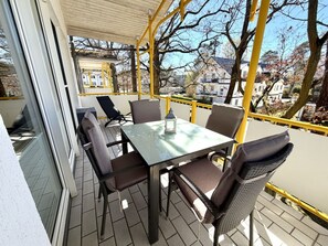 A covered outdoor patio with a table and chairs, a view of the surrounding area, and a yellow railing. - Holiday Apartment Kustennest Baabe (Ostseebad Baabe)