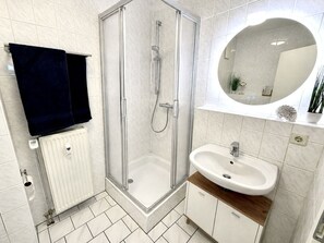 A modern bathroom with a glass-enclosed shower, a white sink, and a mirror above the sink. - Holiday Apartment Kustennest Baabe (Ostseebad Baabe)