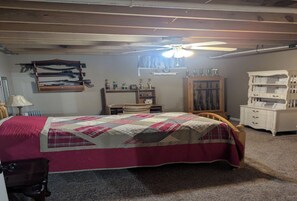 Een slaapkamer met een bed, een houten hoofdbord, een plafondventilator, een dressoir en een kast.