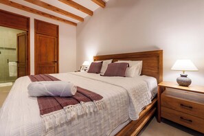 A neatly made bed with a white comforter and patterned pillows, a wooden nightstand with a lamp, and a wooden door with a towel hanging on it. - CASA CAOBA - Modern colonial Villa, 3 volcano views rooftop & 4BR (Antigua)
