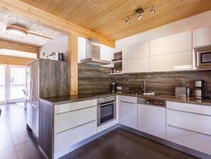 Eine moderne Küche mit Holzbalkendecke, Edelstahlgeräten und einer großen Kochinsel mit integriertem Backofen.