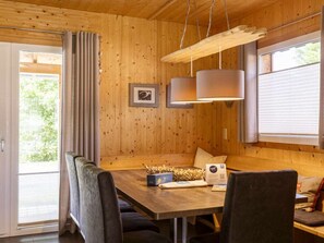A wooden interior with a dining table, chairs, a hanging light fixture, and a window with blinds. - One-bedroom Cabin (Sankt Georgen am Kreischberg)