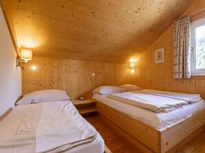 Ein Zimmer mit zwei Holzbettställen, einem Nachttisch, einer an der Wand befestigten Lampe und einem Fenster mit Vorhängen.