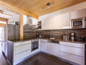 A modern kitchen with stainless steel appliances, wooden ceiling beams, and a dark backsplash. - One-bedroom Cabin (Sankt Georgen am Kreischberg)