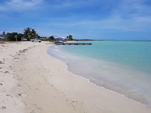 Uma praia com céu claro, areal arenoso e um barco na água.