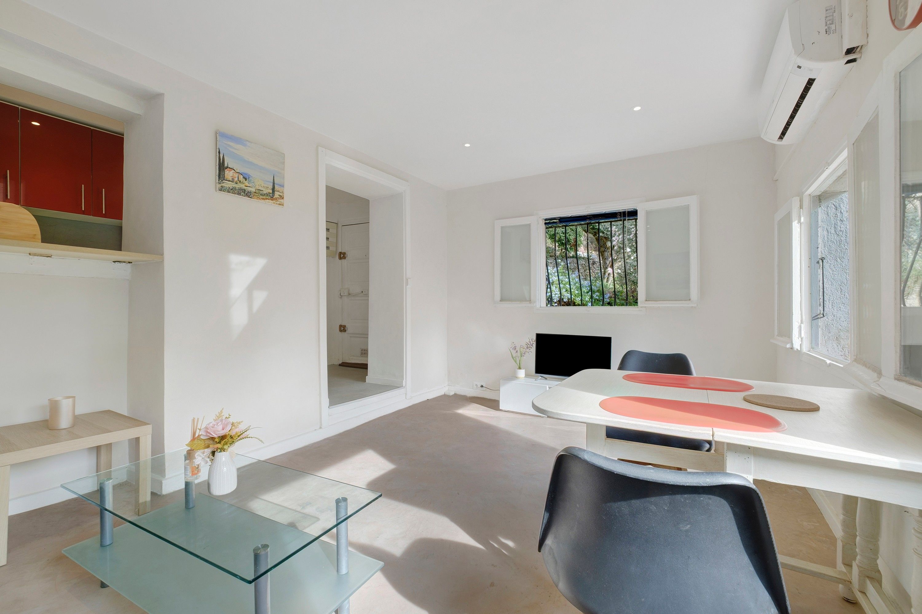 Una sala de estar moderna y minimalista con una mesa de centro de vidrio, un televisor de pantalla plana y un comedor con una mesa blanca y sillas rojas.