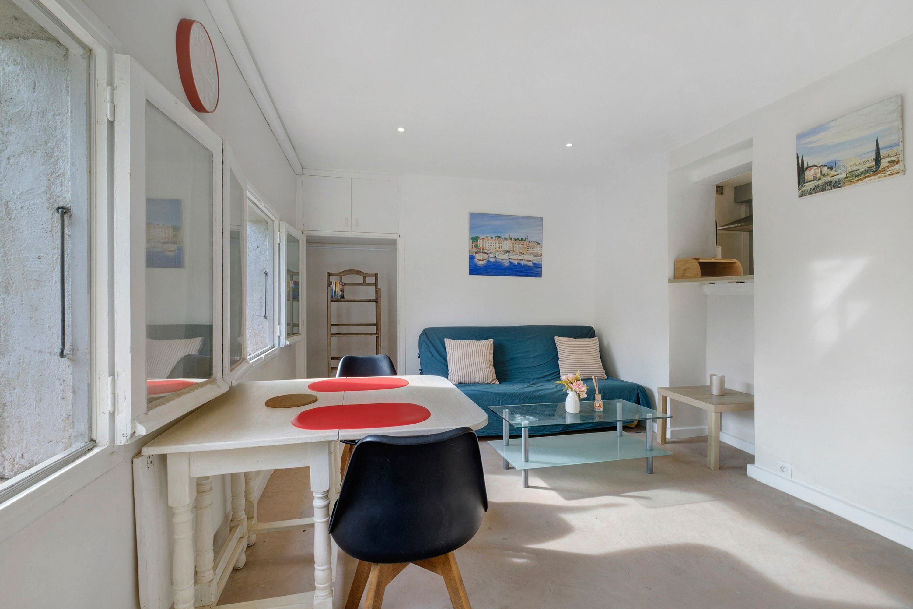 Un salon moderne comprenant un coin repas, un canapé bleu, une table basse en verre et un tableau accroché au mur.