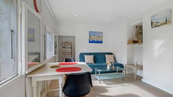 Un salon moderne comprenant un coin repas, un canapé bleu, une table basse en verre et un tableau accroché au mur.