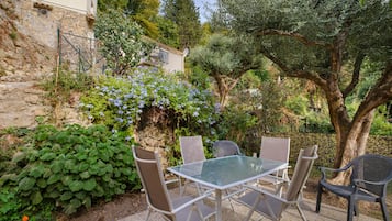 Een terras met een tafel en stoelen, omringd door groen en een stenen muur.