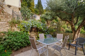 An outdoor seating area with a table and chairs, surrounded by greenery and a stone wall.