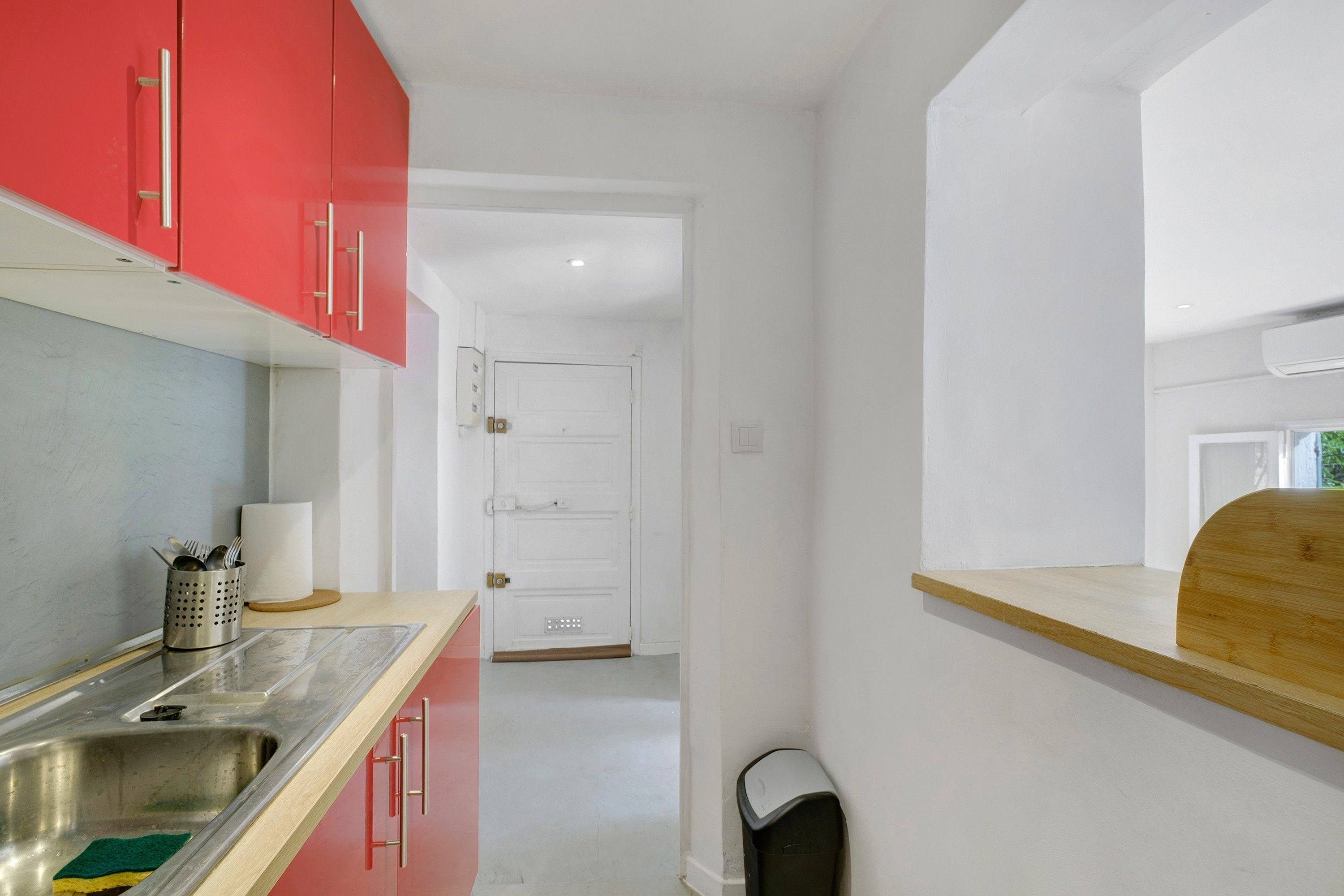 Une cuisine avec des meubles de rangement rouges, un évier en acier inoxydable et un plan de travail en bois.