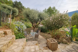 Jardí amb taula i cadires, envoltat de plantes i arbres diversos.