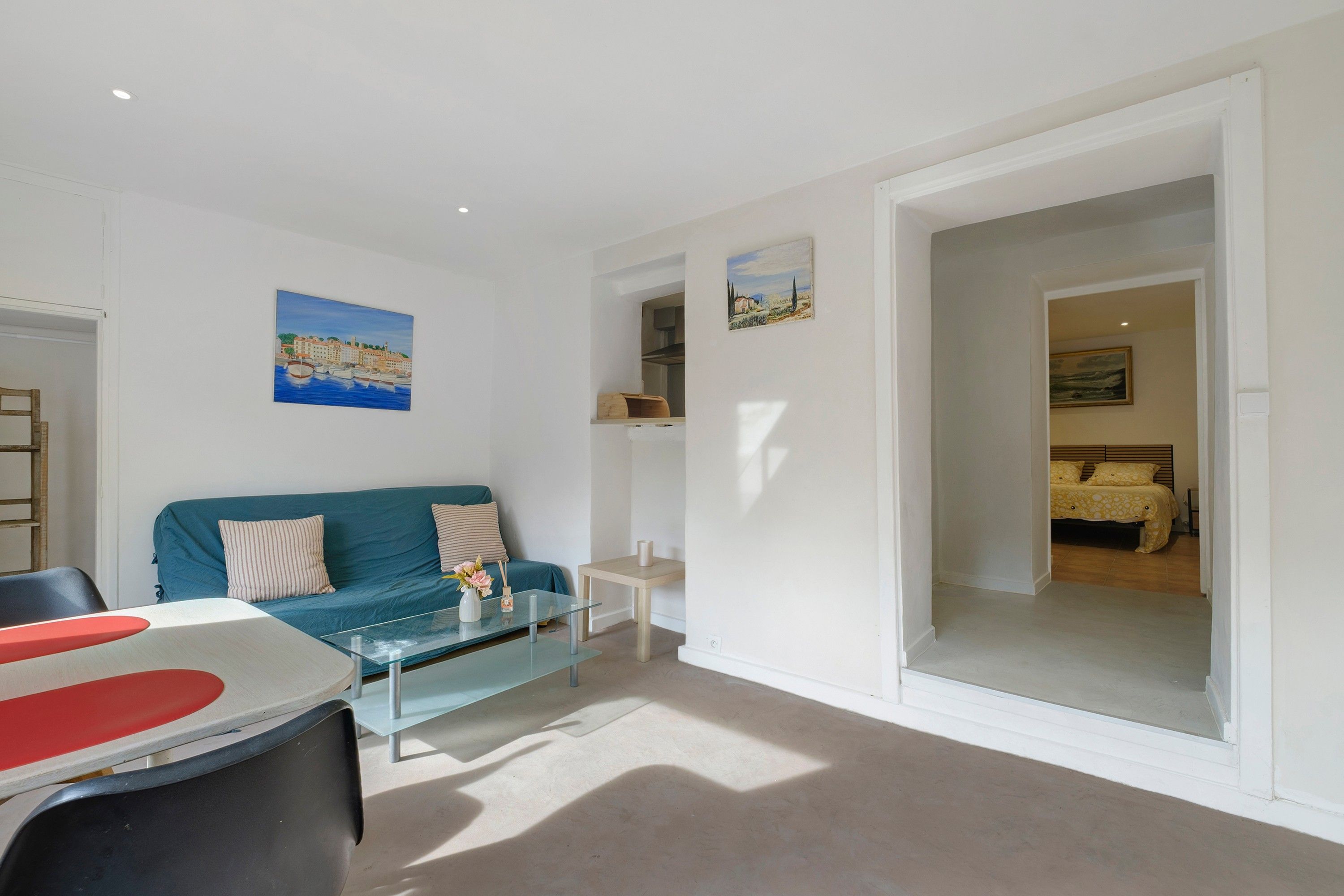 A modern living room with a blue sofa, a glass coffee table, and a painting of a coastal scene.