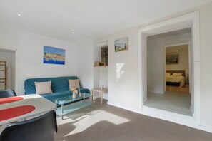 A modern living room with a blue sofa, a glass coffee table, and a painting of a coastal scene.