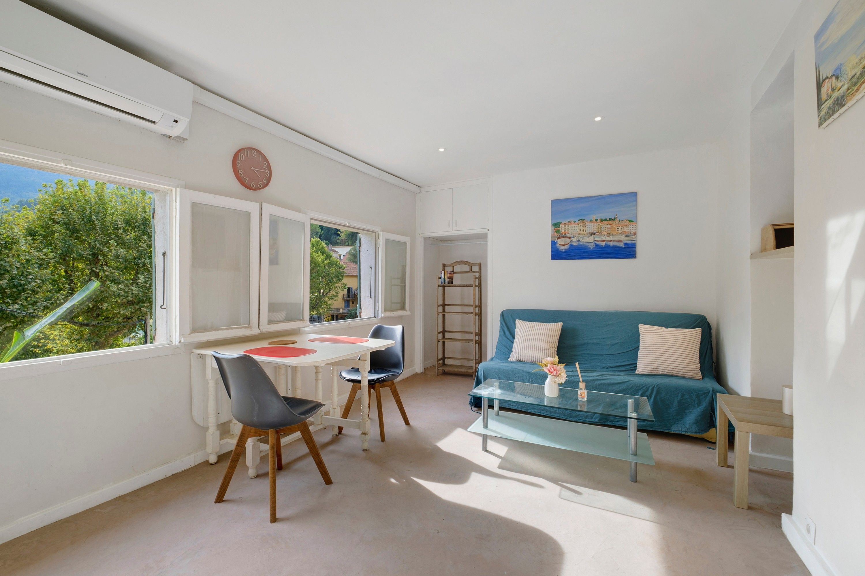 Un salon moderne avec une table basse en verre, un canapé bleu et un coin repas comprenant une table et des chaises blanches.