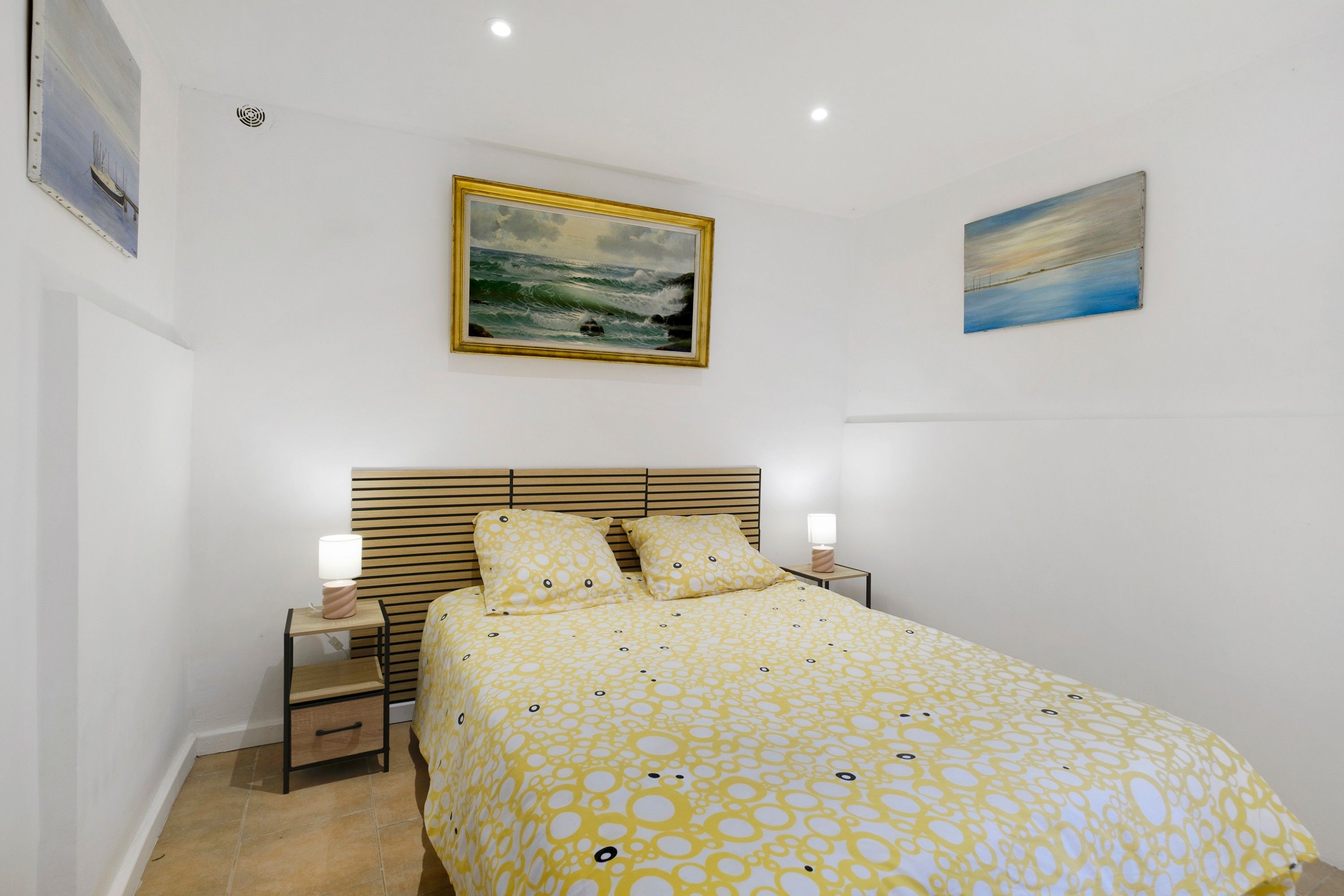 Een slaapkamer met een bed, twee nachtkastjes, een hoofdbord en twee aan de muur bevestigde schilderijen.
