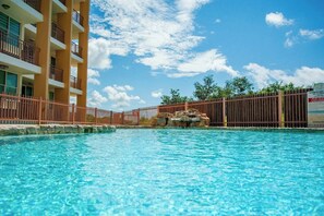 A swimming pool with clear blue water, surrounded by a wooden fence and a multi-story building with balconies. - Ocean View Condo with Pool Near El Combate Beach (Boquerón)