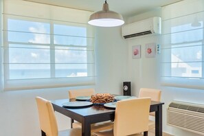 A dining area with a table set for four, a hanging pendant light, and an air conditioning unit on the wall. - Ocean View Condo with Pool Near El Combate Beach (Boquerón)