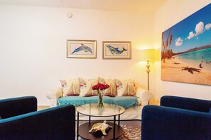Ein Wohnzimmer mit einer Couch, zwei gerahmten Gemälden von Delfinen, einer Lampe und einem Strandbild.