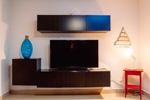 Ein modernes Wohnzimmer mit einem Flachbildfernseher, einer dunkelholzigen Unterhaltungseinheit, einer blauen Vase und einem kleinen roten Tisch mit einer Lampe.