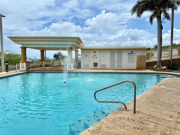 A swimming pool with a fountain, a covered area, and a building with a sign. - Beachside Condo with Pool and Ocean Views (Pole Ojea)