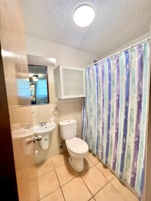 A bathroom with a toilet, sink, and shower curtain. - Beachside Condo with Pool and Ocean Views (Pole Ojea)