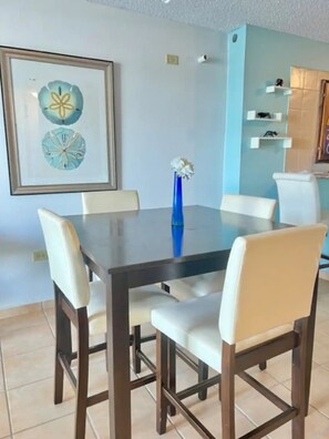 A dining area with a table and chairs, a framed artwork on the wall, and a vase with flowers. - Beachside Condo with Pool and Ocean Views (Pole Ojea)
