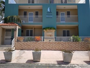 Ein mehrstöckiges Gebäude mit Balkonen, einem Schild mit der Aufschrift 'Condominio El Veleiro' und Blumentöpfen im Vordergrund.