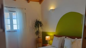 A bedroom with a bed, a nightstand, a lamp, a potted plant, and a window with curtains. - Apartment 'Casa Oliveira' with Mountain View, Wi-Fi and Air Conditioning (Melides)