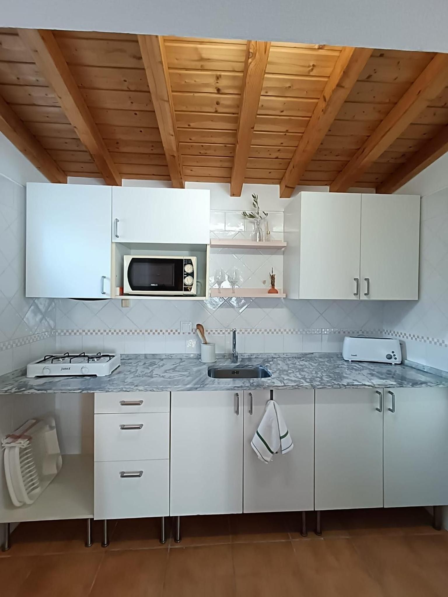 Cozinha moderna com armários brancos, micro-ondas embutido, fogão a gás e painel de azulejos.