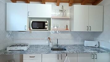 Cozinha moderna com armários brancos, micro-ondas embutido, fogão a gás e painel de azulejos.