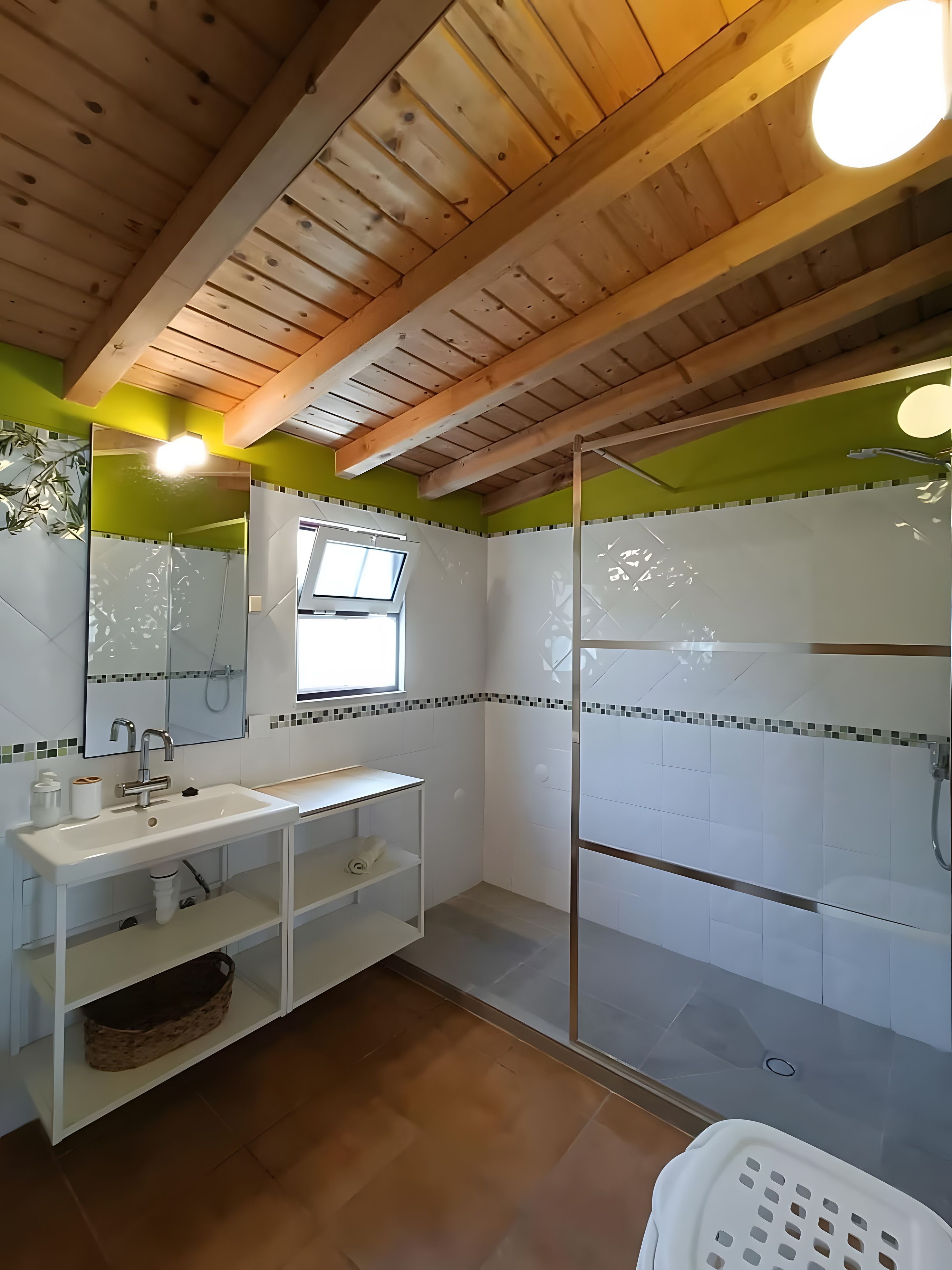 Ein Badezimmer mit Holzboden, einem weißen Waschbecken mit Spiegel, einer Duschkabine und einem Fenster.